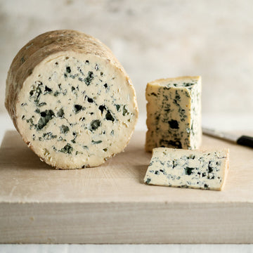 Large and small cuts of Fourme d'Ambert blue cheese on a wooden board.