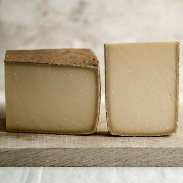 Two cut pieces of Gruyere hard cow's milk cheese on a wooden board.