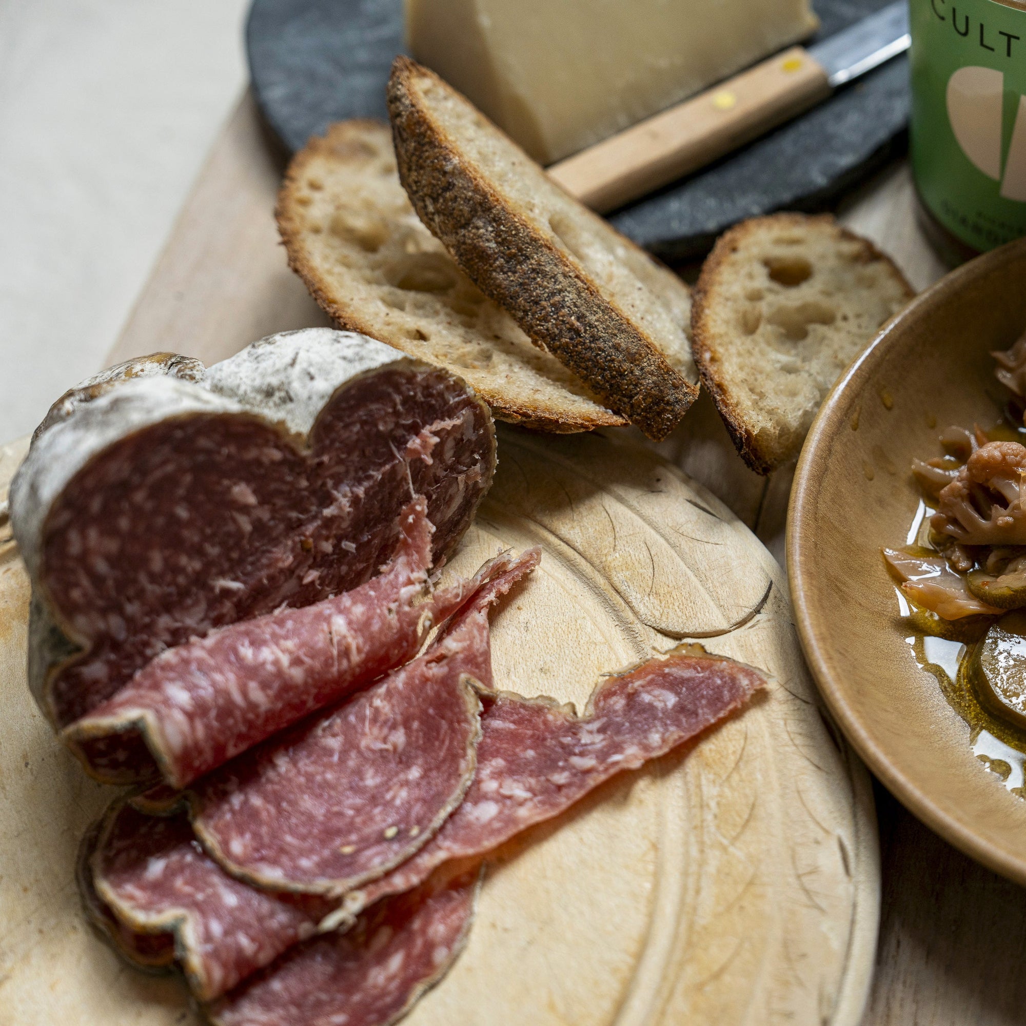Slices of 'Jesus' salami with some slices of bread on a wooden board.