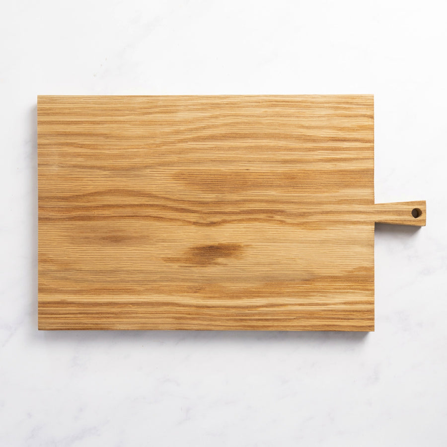 A rectangular wooden chopping board with a small handle at one end on top of a marble worktop.