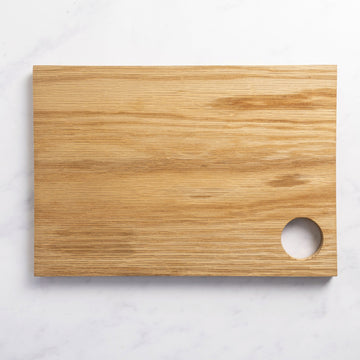 A ractangular wooden board with a thumb-hole in one corner, on a marble worktop.