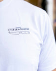 The chest of a man in a white t-shirt wih a straight London Cheesemongers and knife logo over the breast area.