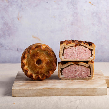 A cut and whole pork pie on a wooden chopping board.