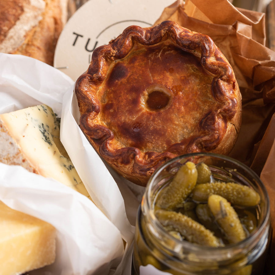 A selection of cheeses, cornichons and a pork pie.