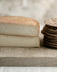 A cut Riseley ewe's milk cheese with some savoury biscuits on a wooden board.