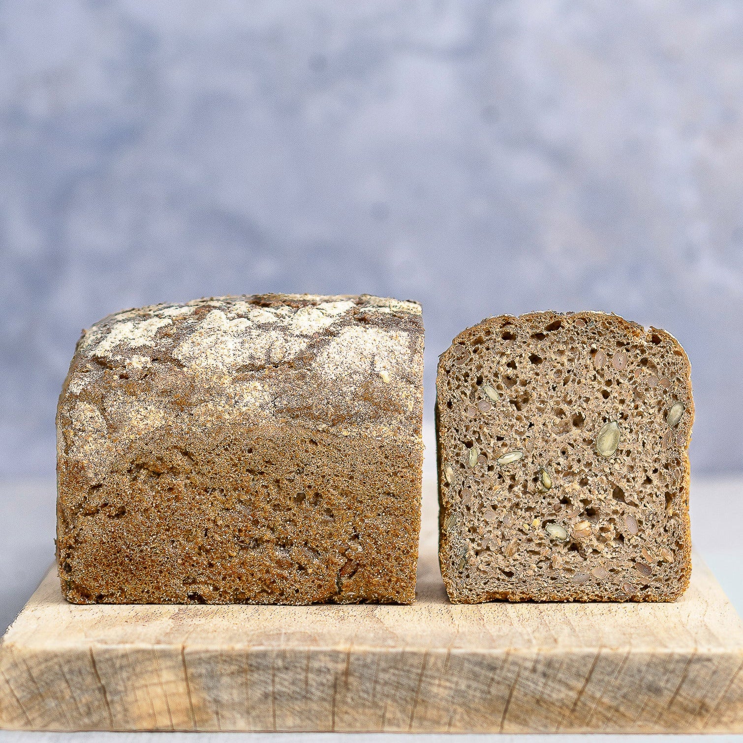 A rye loaf of bread cut in half and on a wooden board. 