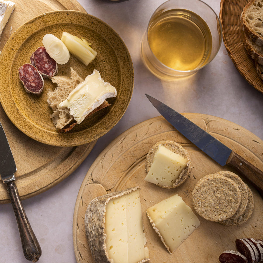 A selection of cheese, charcuterie and biscuits, with a glass of white wine, on a table top.