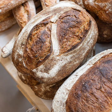 Loaves of brown sourdough bread stacked up on a table.