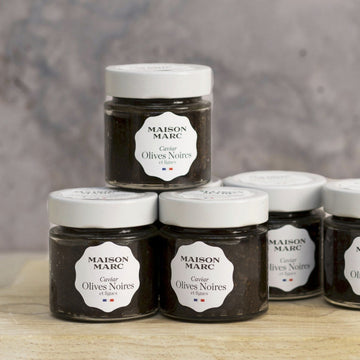 Jars of maison marc tapenade of black olive on a wooden board.