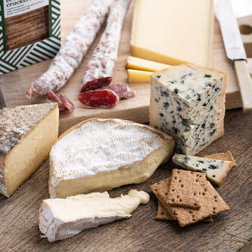 A selection of cuts of French cheese on a wooden board with charcuterie and biscuits.