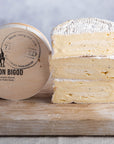 Cuts of Baron Bigod truffle cheese and its box on a wooden board.