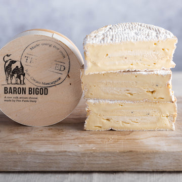 Cuts of Baron Bigod truffle cheese and its box on a wooden board.