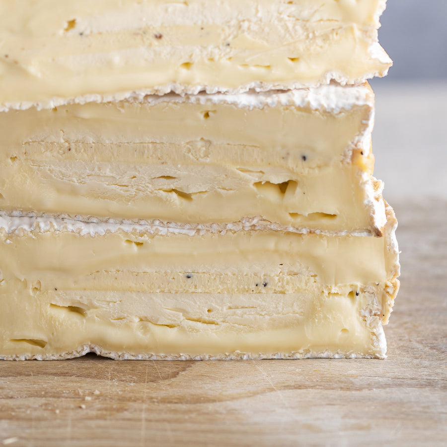 A close up of the cut side of baron bigod truflled cheeseon a wooden board.