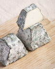 A cut and whole pieces of blackmount goat cheese on a wooden board.