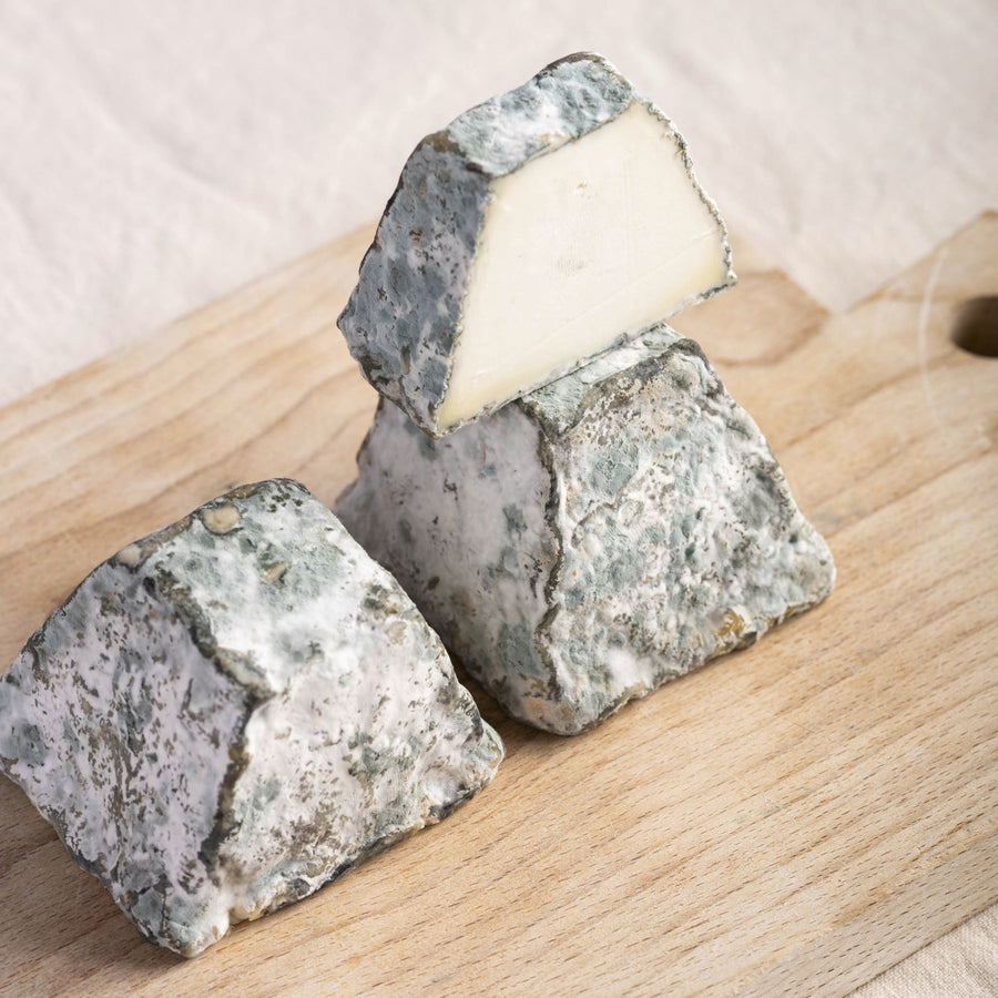 A cut and whole pieces of blackmount goat cheese on a wooden board.