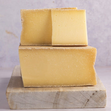 Large cuts of Branzi hard cow's milk cheese on a wooden board.