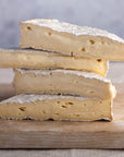 Stack of four cut pieces of Brie cheese on a wooden board.