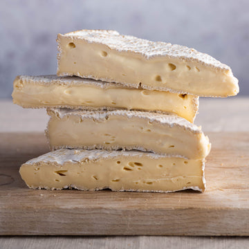 Stack of four cut pieces of Brie cheese on a wooden board.