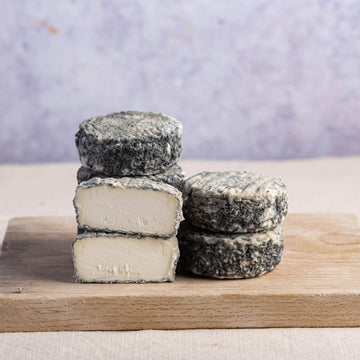 Cut and whole pieces of brightwell ash goat cheese stacked up on a wooden board.