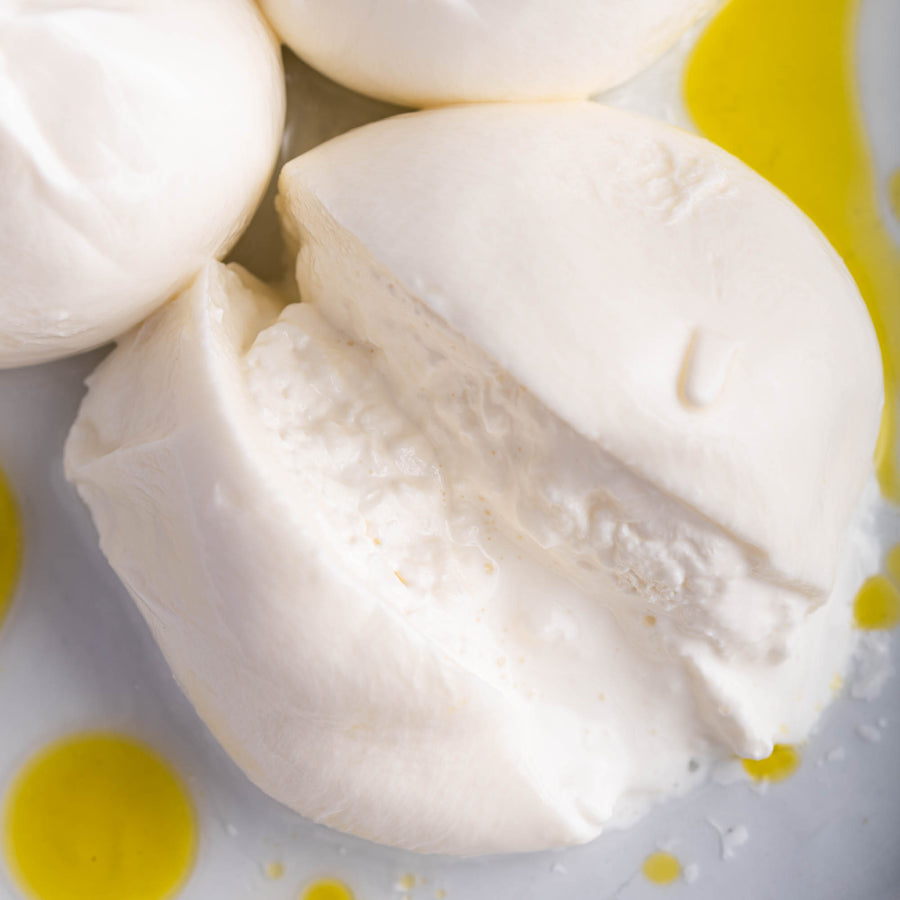 A cut Burrata cheese on a plate drizzled with some olive oil.