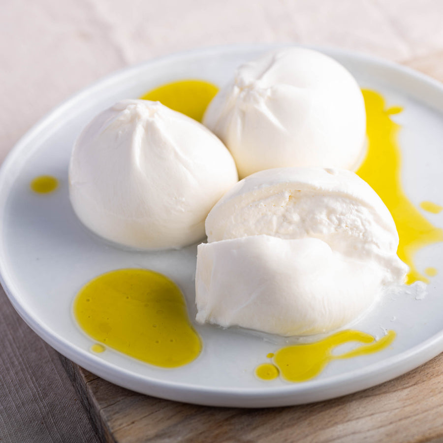 Balls of whole and cut Burrata cheese on a plate drizzled with some olive oil.