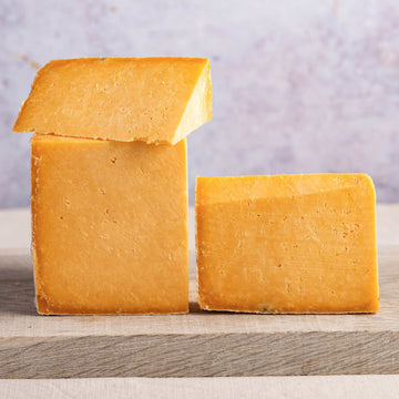 Cut pieces of orange cheshire cheese on a wooden board.