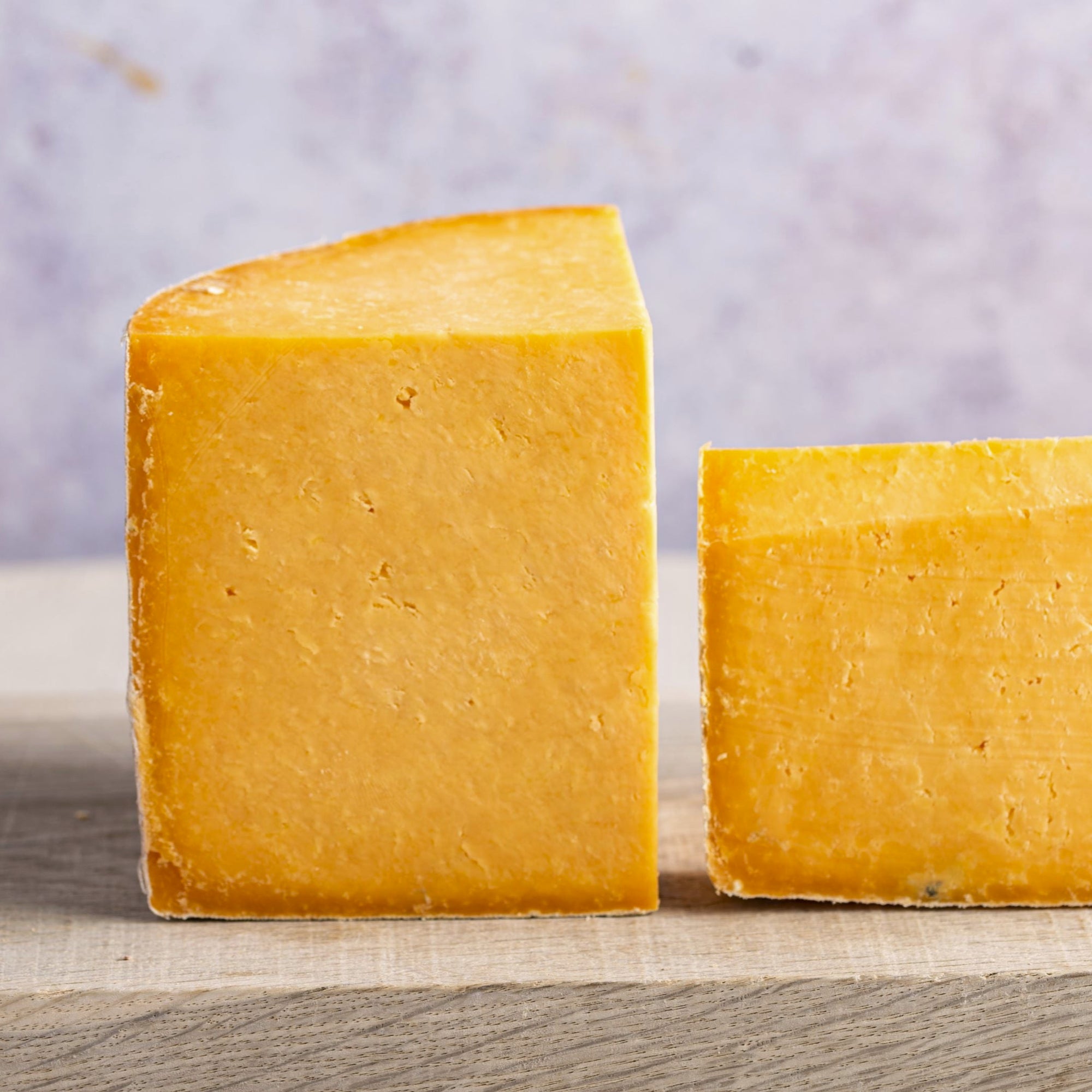 Two cut pieces of orange cheshire cheese on a wooden board.