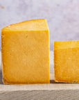 Two cut pieces of orange cheshire cheese on a wooden board.