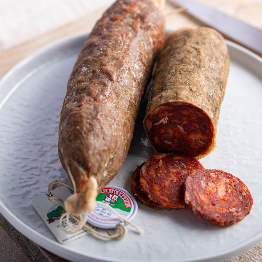 Slices and a whole chorizo spicy sausage on a white plate.