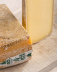 A cut and larger piece of comte cheese on a wooden board.