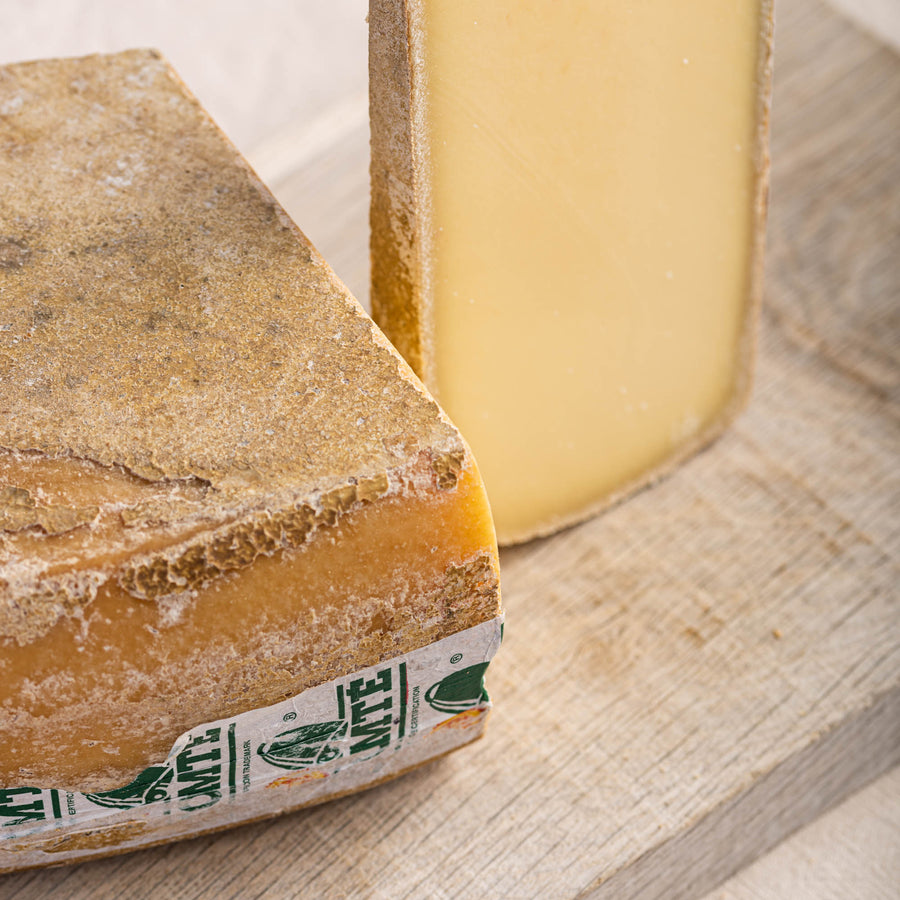 A cut and larger piece of comte cheese on a wooden board.