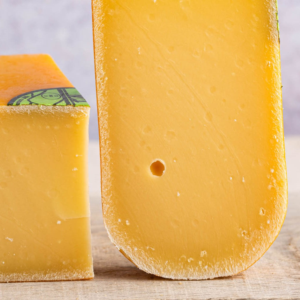 A close up of the cut face of a piece of Coolea cheese on a wooden board. 