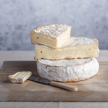 Cuts of Coulommiers on a whole cheese on a wooden board.