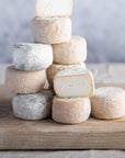 A pile of cut and whole Crottin de Chavignol goat's cheeses on a wooden board.