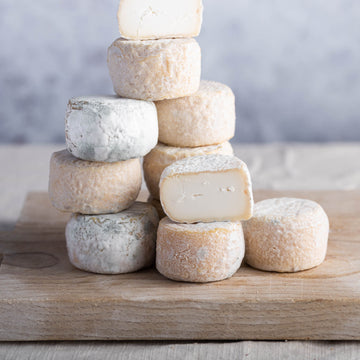 A pile of cut and whole Crottin de Chavignol goat's cheeses on a wooden board.