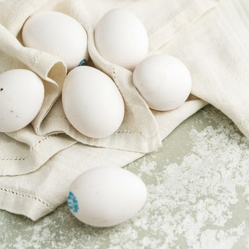 Some white Cacklebean hen's eggs on a table cloth on a worktop.