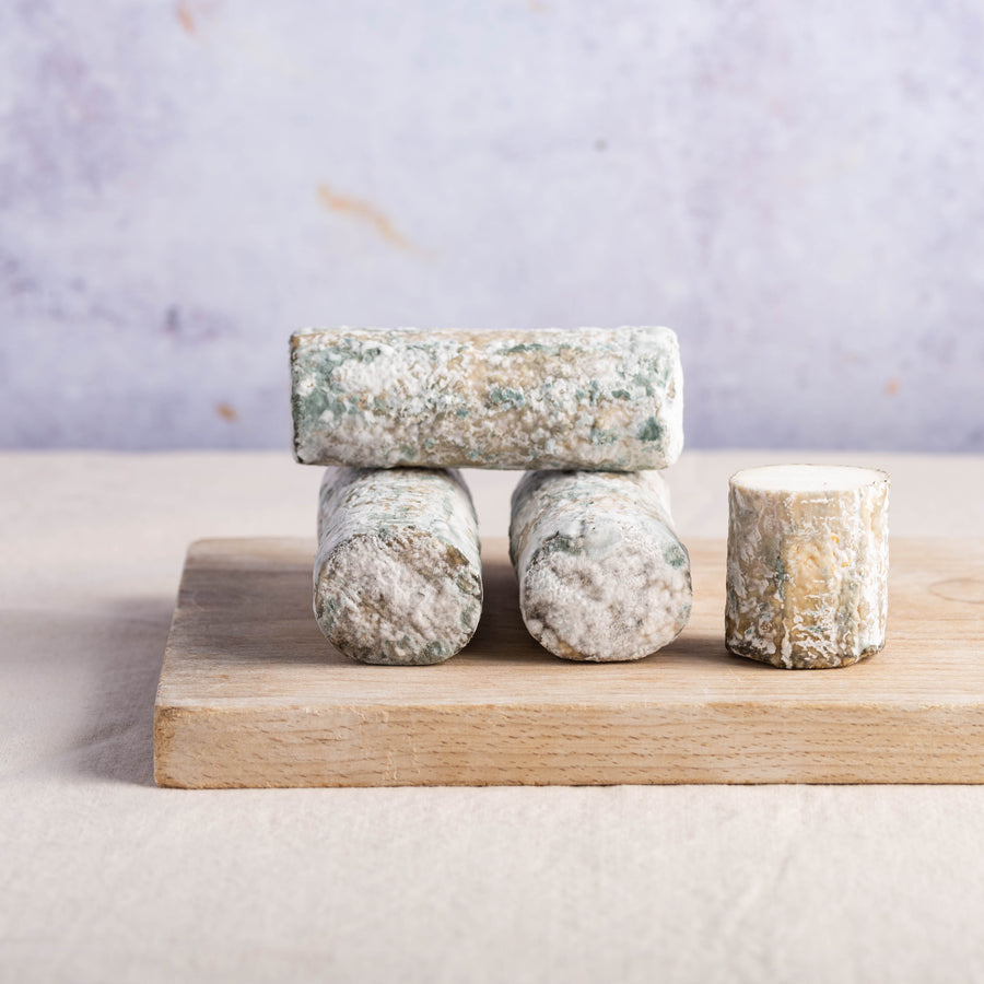 Whole and cut pieces of Elrick Log goat's cheese on a wooden board.