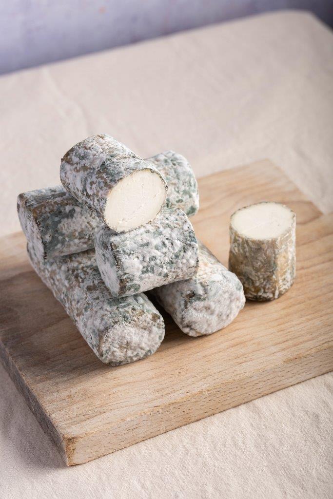 An overhead shot of cuts and whole pieces of Elrick Log goat's cheese on a wooden board.