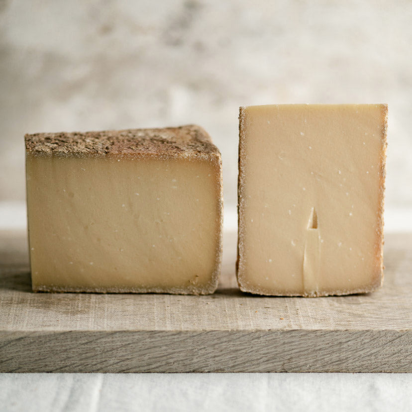 Two pieces of cut L'Etivaz swiss hard cheese on a wooden board.