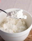 Goat's curd being spooned out of a white ceramic bowl.