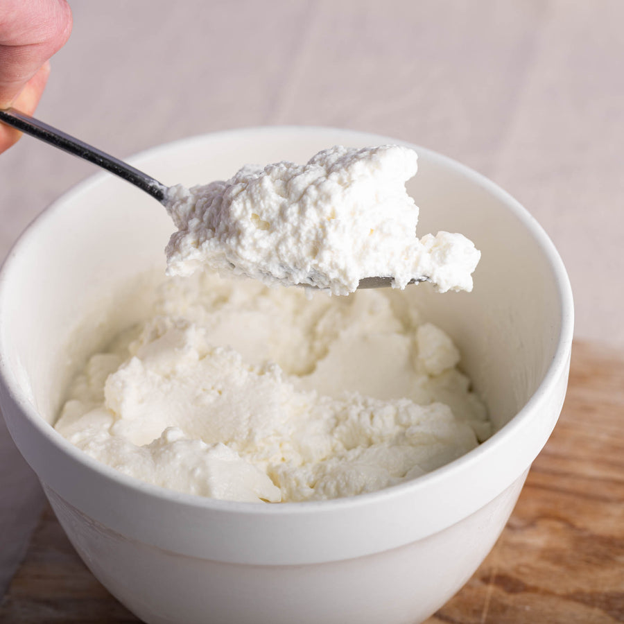 Goat's curd being spooned out of a white ceramic bowl.