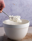 A hand spooning some white goat's curd out of a bowl.