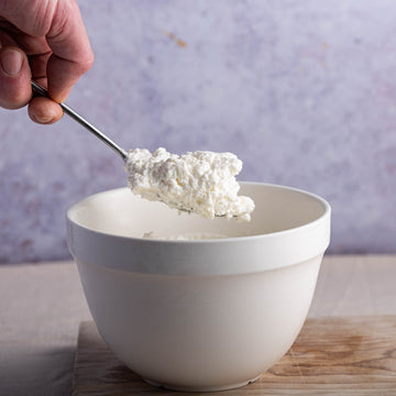 A hand spooning some white goat's curd out of a bowl.
