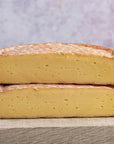 Two cut halves of gubbeen chees stacked on a wooden board.