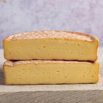 Two cut halves of gubbeen chees stacked on a wooden board.