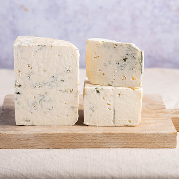 Cut pieces of harbourne blue cheese on a wooden board.