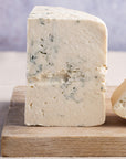 Close up of the cut side of a piece of Harbourne Blue cheese on a wooden board.