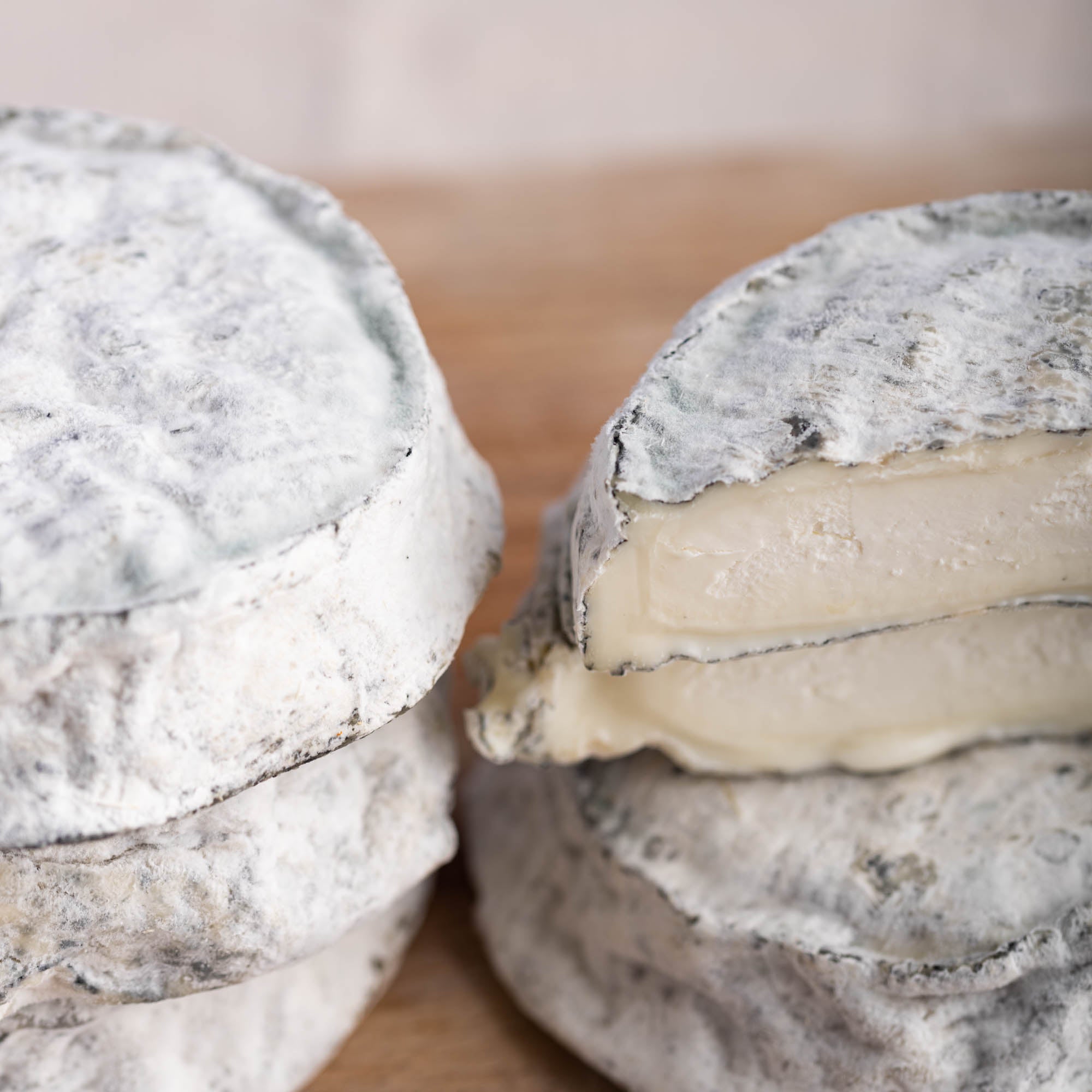 A close up shot of whole and cut pieces of selles sur couffy goat's cheese on a wooden board.