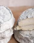A close up shot of whole and cut pieces of selles sur couffy goat's cheese on a wooden board.