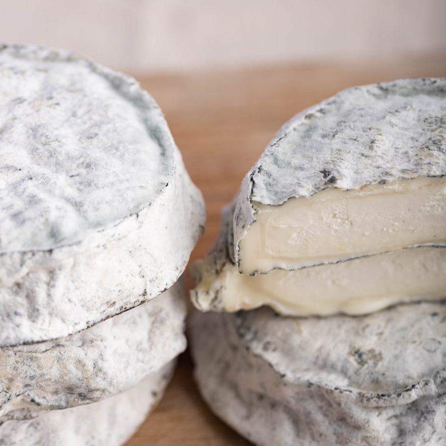 A close up shot of whole and cut pieces of selles sur couffy goat's cheese on a wooden board.